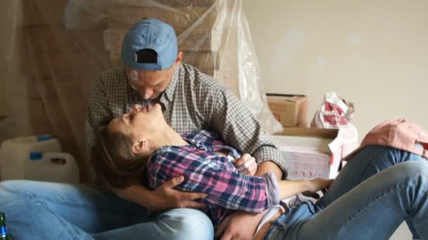 Retrato de una hermosa pareja de ojos azules marido y mujer en su nuevo apartamento durante la renovación. El chico y la chica se abrazan y besan, sus caras están manchadas de pintura. Reparación romántica — Vídeo de stock