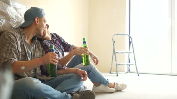 Guy e menina bebem cerveja enquanto relaxam após o reparo. Housewarming, recém-casados fazer reparos — Vídeo de Stock