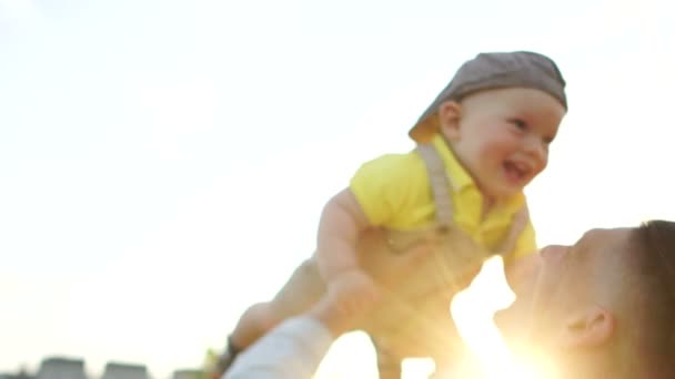 Día de los padres, concepto familiar. Un feliz padre joven arroja a su bebé en el fondo del cielo del atardecer y los rayos del sol — Vídeos de Stock