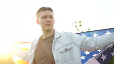 Amerika Birleşik Devletleri bayrağıyla günbatımının tadını çıkaran genç ve ciddi bir adam. Vatanseverlik Günü, Usa Bağımsızlık Günü, 4 Temmuz Kutlaması