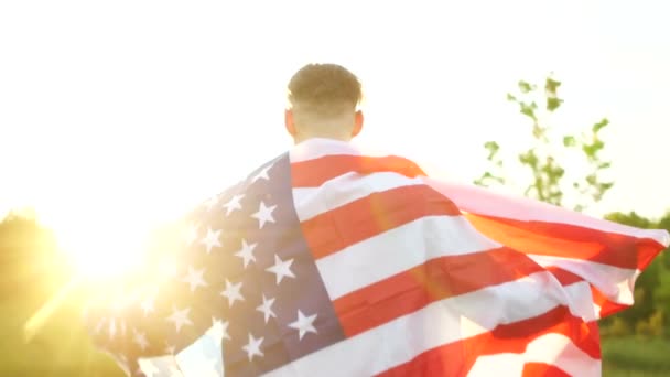 Jour de l'indépendance, le 4 juillet. Vue arrière d'un grand drapeau américain sur les épaules d'un homme. La mémoire des soldats américains morts, un jour patriotique — Video