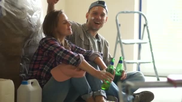 Housewarming, de nygifta göra reparationer. Killen och flickan dricker öl under resten efter reparationen. Hem renovering, fastighet, DIY, gör det själv — Stockvideo