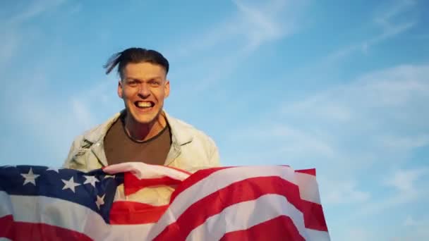 Патріотичний день. Молода активна людина в джинсовому піджаку з прапором Сполучених Штатів в його руках кричить скандували Сполучені Штати — стокове відео