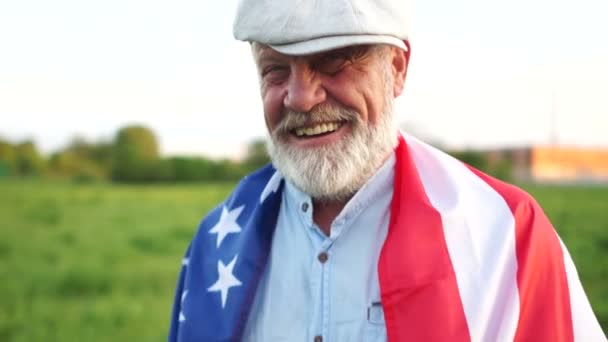 Homme mûr dans un chapeau et une barbe grise pensionné avec drapeau américain dans le parc le jour ensoleillé. Jour de l'indépendance des États-Unis, jour patriotique — Video