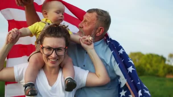 American citizens celebrate Independence Day. Three generations of the same family, grandfather, daughter and little grandson hold the flag of the USA — Stock Video