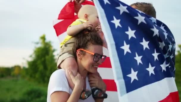 Krásný americký rodinný výlet na 4. Dědeček hraje s vnukem. Dítě sedí na maminky, na ramenou je americká vlajka — Stock video