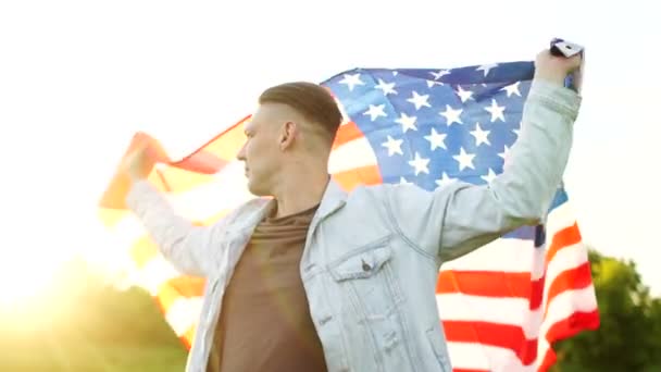 Young serious man in a denim jacket with an American flag in his hands. Patriotic day, independence day — Stock Video