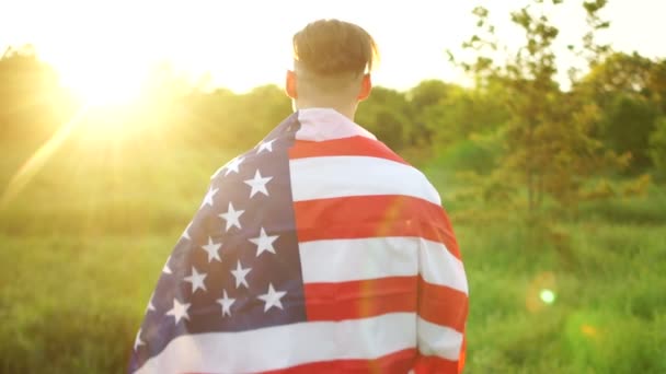 Visão traseira de uma grande bandeira americana nos ombros de um homem. A memória dos soldados americanos mortos, um dia patriótico. Dia da Independência, 4 de Julho — Vídeo de Stock