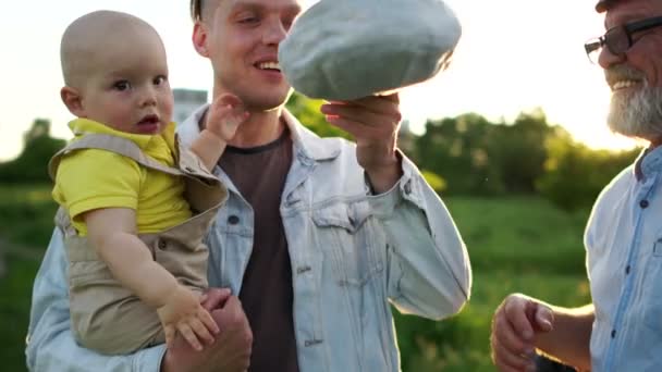 Familj med flera generationer. Morfar pensionerade, vuxen son och år gamla barnbarn leker med en mössa. Tre män vilar på naturen. Färgglada solnedgången — Stockvideo