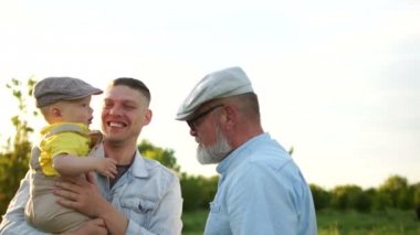 Mutlu bebek ailesi, babası ve dedesi ile parkta bir yürüyüş. Çocuk büyükbabasının şapkasını çıkarır. Güzel gün batımı, güneş parlaması, aile konsepti