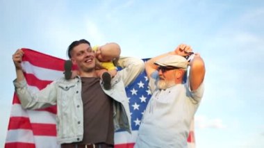 Amerikalı bir aile, üç nesil, büyükbaba, oğul ve torunu bir Amerikan bayrağı tutuyorlar. Dış mekan portresi. Bağımsızlık Günü, 4 Temmuz