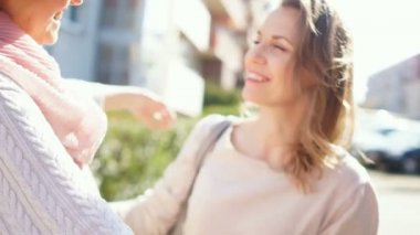 Anne ve yetişkin kızı güneşli, rüzgarlı havalarda sokakta birbirlerine sarılmak. Ağaçlar etrafında çiçek