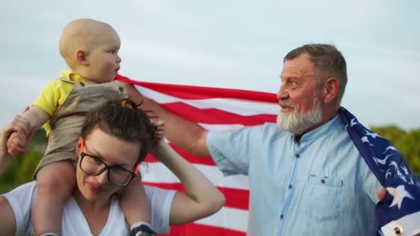 Família feliz segurando bandeira americana no parque em um dia ensolarado. Retrato ao ar livre. Dia da Independência, 4 de julho — Vídeo de Stock