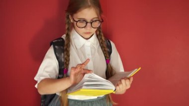 Gözlüklü kız öğrenci kitabı dikkatlice saçıyor. Kırmızı arka planda kız öğrenci