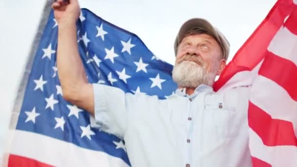 Close portrait of an elderly man with a flag of the USA. The pensioner looks up and smiles. Independence Day — Stock Video