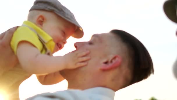 Schöner Vater wirft seinen glücklich lachenden Sohn bei schönem Sonnenuntergang in den Park — Stockvideo