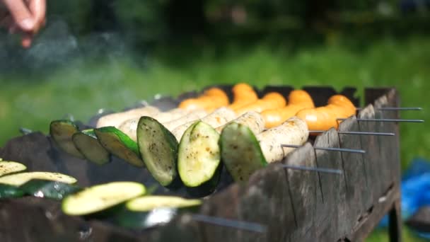 Asar salchichas y verduras a la parrilla en la barbacoa. Manos de un hombre irreconocible girando las salchichas en pinchos — Vídeos de Stock