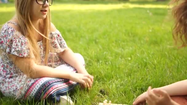 Deux copines adolescentes jouant aux échecs dans le parc assis sur l'herbe. Vacances scolaires, jeux intellectuels pour adolescents — Video