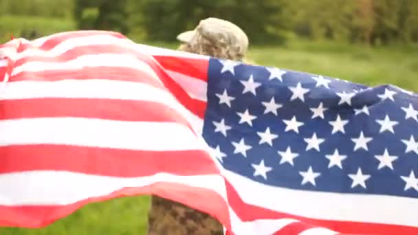 Schoolboy tonåring i kamouflage och med en amerikansk flagga som går genom parken. USA självständighetsdagen firande 4 juli — Stockvideo