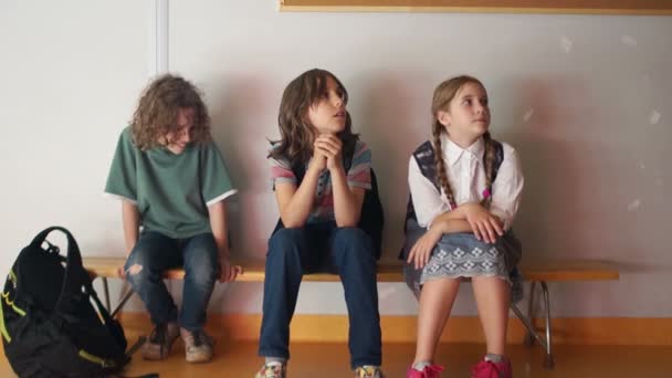 Trzy nastolatków w szkole siedzieć na ławce i nudzić. Nierozpoznawalny nauczyciel dorosły prowadzi i wita uczniów w podróży. Dzieci są szczęśliwe i uśmiechnięte — Wideo stockowe