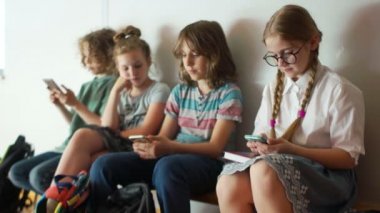 Gençler ve akıllı telefonlar. Çocuklar okul molası sırasında akıllı telefonlar kullanır. Bir bankta oturan okul çocuk bir grup, Internet bağımlılığı