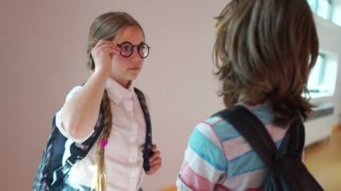 Beautiful schoolgirl with glasses and two cute pigtails and a backpack talking in the school hallway with a classmate. Back to school