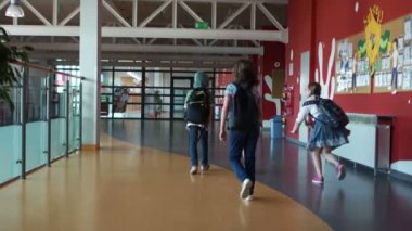 Çocuklar okul binasında koridorda yürüyebilir. Okul molası, sırtlarında arka çantalar ile gençler bir grup, arka görünüm, kapalı