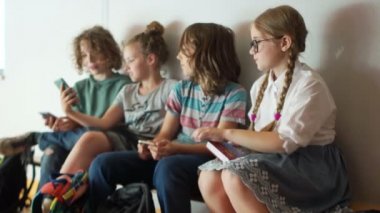 Çocuklar okul koridorunda bir bankta oturur. İki sınıf arkadaşı birbirlerine bir akıllı telefon, okul dostluk göstermek