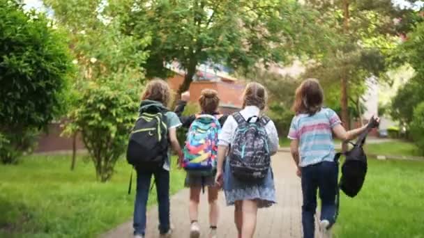 As crianças se divertem correndo para fora da escola, balançando mochilas sobre suas cabeças. O início das férias de verão, o fim do ano letivo — Vídeo de Stock