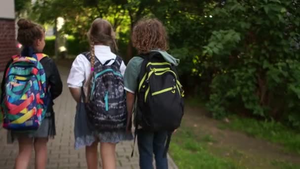 Drei Teenager gehen auf den Straßen der Stadt an Autos vorbei zur Schule. Rückseite, zurück zur Schule, Klassenkameraden-Freundschaft — Stockvideo