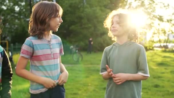 Δύο αγόρια και ένα κορίτσι έφηβοι μιλούν στην παιδική χαρά στο ηλιοβασίλεμα. Επιστροφή στο σχολείο, σχολική φιλία και επικοινωνία — Αρχείο Βίντεο