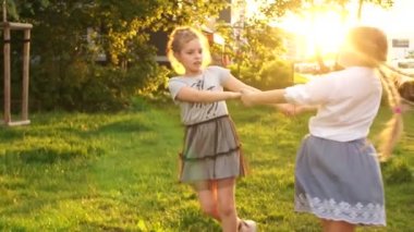 İki kız etrafta koşuşturuyor, parkta çimlerin üzerinde dönüyorlar, ormanda. Mutlu çocuklar, okul tatilleri, gün batımı ışınları