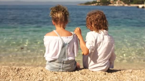 Un par de adolescentes, un niño y una niña, sentados abrazándose en la orilla del hermoso mar claro, vista trasera. Amor, concepto de amistad — Vídeo de stock