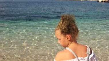 Kız genç plajda oturur ve suya çakıl taşları atar. Güzel doğa ve berrak turkuaz su. Seyahat konsepti