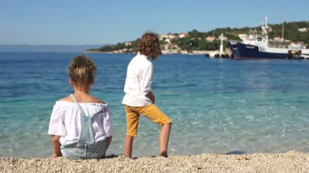 Вид сзади, школьники кудрявый мальчик и девочка играют друг с другом на берегу Средиземного моря. Адриатика, Хорватия, регион Долмации. Концепция путешествия — стоковое видео