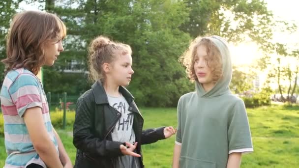 Τρεις έφηβοι φίλοι μιλούν ενώ στέκονται στο πάρκο. Μια τέταρτη φίλη τους έρχεται. Καλή παιδική ηλικία, πίσω στο σχολείο — Αρχείο Βίντεο