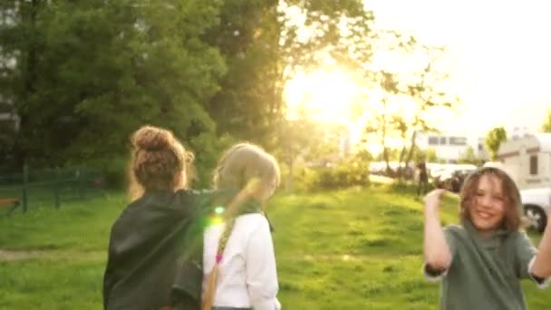 Três crianças, duas meninas e um menino vão para a distância no parque contra o pano de fundo do pôr do sol. De volta à escola, crianças felizes, amizade na escola — Vídeo de Stock