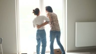 Yeni evliler, pencerenin yanında ayakta sarılma konusunda mutlu. Emlak Kiralama, ev satın alma, genç aileler için krediler