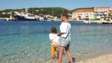Kıvırcık çocuk çocuk ve kız açık deniz suyu içine çakıl atmak. Adriyatik kıyısı, Slovenya, Dalmaçya, Akdeniz kıyısı
