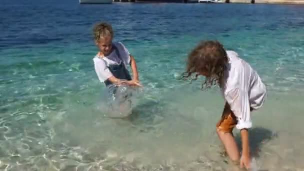 Curly menino e menina diversão salpicando água, de pé em roupas no mar. adriático, feriados na Croácia, feriados com crianças, feriados infantis, feriados escolares — Vídeo de Stock