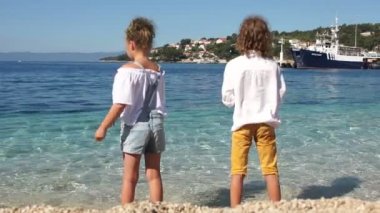 Kardeş, öğrenciler, Hırvat kasabasının arka planında ve yatlar ile deniz iskelesinin açık mavi deniz suyuna taş atıyorlar. Adriyatik kıyısı, Slovenya, Dalmaçya, Akdeniz kıyısı