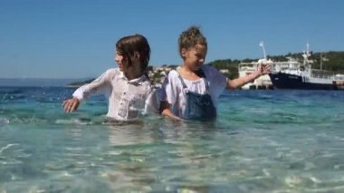 Islak kıvırcık çocuklar, kardeş ve kız kardeş, farklı yönlerde su sıçramak, giysilerin suda bel ayakta. Çocuklar ve deniz, yaz tatili ve seyahat konsepti