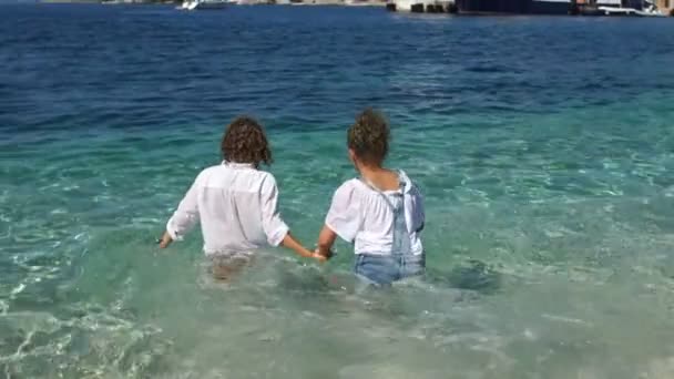 Un par de hermosos niños, un niño y una niña, entran en el agua con ropa. Niños felices, vacaciones con niños — Vídeo de stock