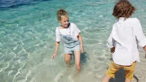 아이들은 야외에서 물놀이를 즐거시합니다. 행복한 아이들은 얕은 물에서 놀고있는 즐거운 어린 소년과 소녀. 여름의 즐거움 — 비디오