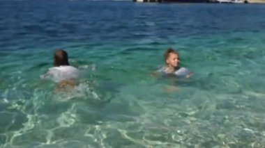 Çocuklar kıyafetleriyle turkuaz deniz suyunda yüzerler. Çocuklarla mutlu tatiller. Seyahat konsepti