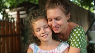 Anne ve kızı, bir köy avlusunda yakın portre. Bir kız ve bir kadın yaz sundresses giymiş, sarılma ve kameraya bakıyor. Anneler Günü