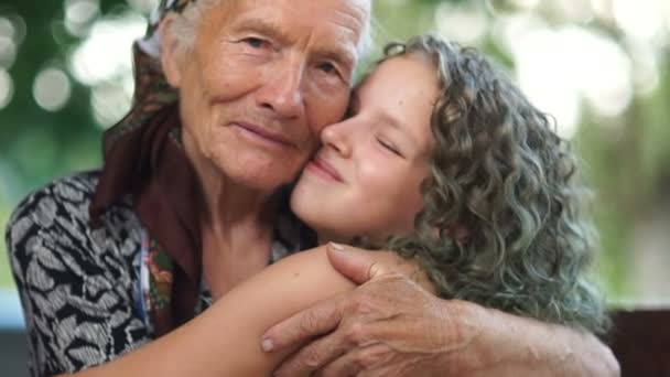 Retrato de perto de uma avó e neta abraçando. Uma mulher idosa com um lenço de cabeça e uma adolescente com cabelo encaracolado tingido. Bisavó e bisneta — Vídeo de Stock