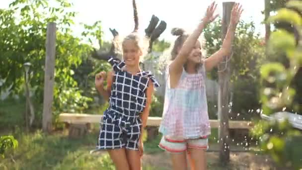 Schulmädchen im Urlaub im Dorf. zwei Mädchen haben Spaß beim Springen unter Wasser, Kinder haben Spaß — Stockvideo