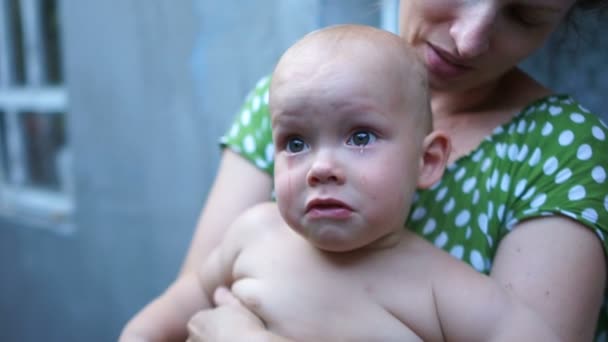 Close portrait of a one year old baby. The child cries while sitting on his mothers lap. Mother calms baby, mothers day, mother and baby — Stock Video