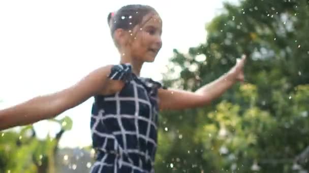 Retrato de una hermosa chica feliz en los rayos del sol poniente. Un niño gira en un aerosol de agua de una manguera — Vídeos de Stock